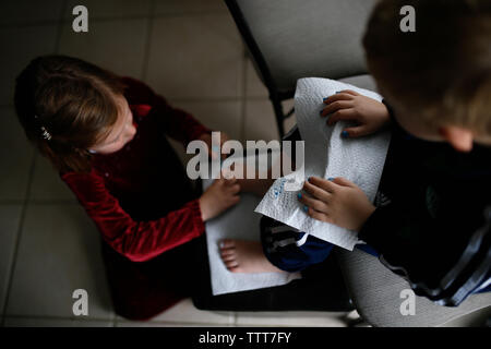 Hohe Betrachtungswinkel der Zehennägel's Schwester Malerei Bruder auf Stuhl zu Hause sitzen Stockfoto