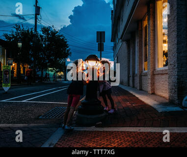 Schwestern auf Lamp Post beim Stehen auf dem Bürgersteig in der Stadt Stockfoto