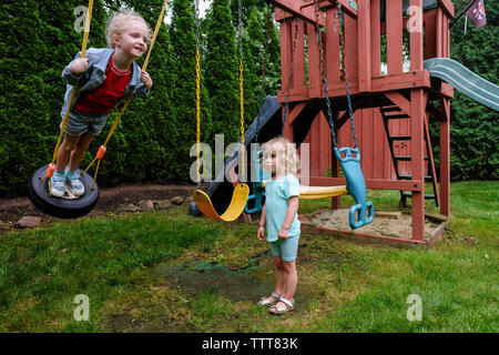 Trauriges Mädchen suchen Bei happy Schwester schwingen auf Reifen Schwingen am Spielplatz Stockfoto