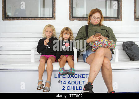 Schwestern sitzen mit Großmutter auf der Fähre Sitzbank gelangweilt Stockfoto