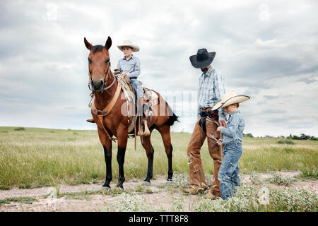 Vater und Söhne mit Pferd auf Feld gegen bewölkter Himmel Stockfoto