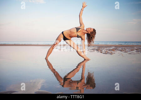 Frau in bikini Yoga am Strand gegen Sky Stockfoto