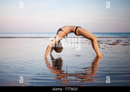 Frau in bikini Yoga am Strand gegen Sky Stockfoto