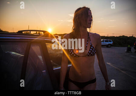 Frau in Bikini stehen mit dem Auto bei Sonnenuntergang Stockfoto