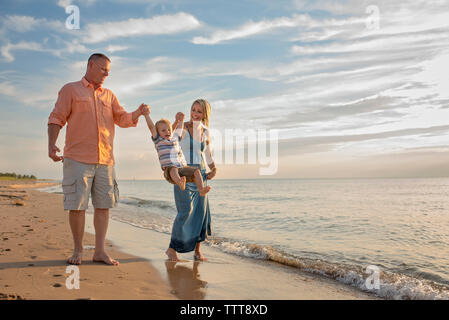 Verspielte Eltern Holding, der Sohn von Händen, während ihn am Strand Schwingen Stockfoto