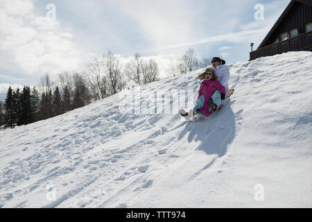 Mutter und Tochter rodeln im winter wonderland an einem sonnigen Tag Stockfoto