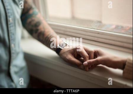 Zugeschnittenes Bild des Paares, Hände auf Fensterbank zu Hause Stockfoto