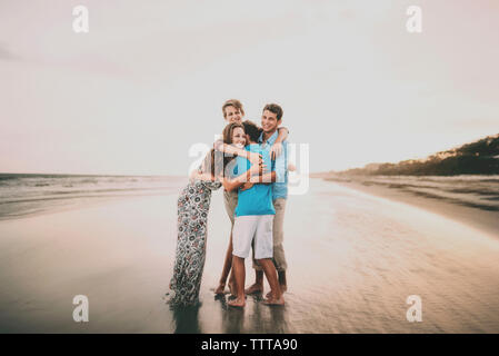 Gerne Geschwister umarmen beim Stehen am Strand gegen Himmel bei Sonnenuntergang Stockfoto