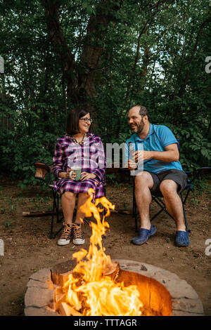 Volle Länge des glücklichen Paare sitzen auf Camping Stühle von Lagerfeuer im Wald Stockfoto