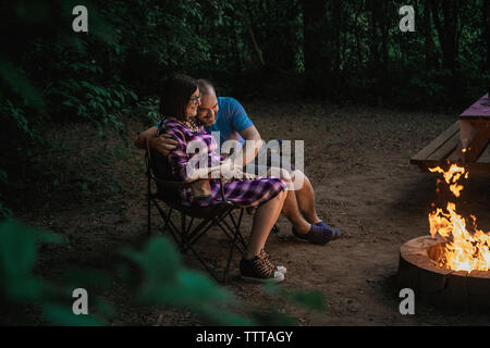 Volle Länge des liebenden Paar sitzt auf Camping Stühle von Lagerfeuer im Wald Stockfoto