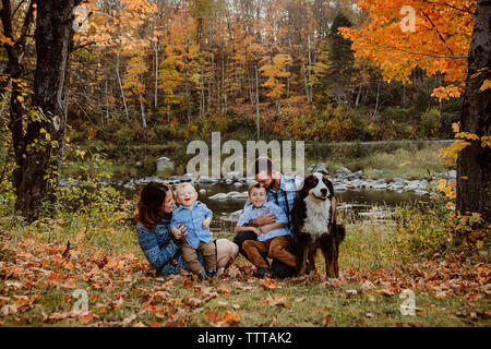 Die Eltern genießen mit Söhnen durch Hund auf Wiese im Wald im Herbst Stockfoto