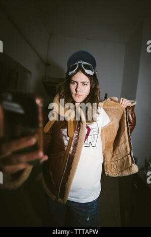 Selbstbewussten jungen Frau mit Motorrad Schutzbrille tragen Leder Jacke während der Einnahme von selfie in Dunkelkammer Stockfoto
