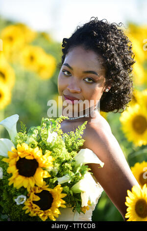 Portrait von Braut holding Blumenstrauß im Stehen gegen Sonnenblumen auf der Farm Stockfoto