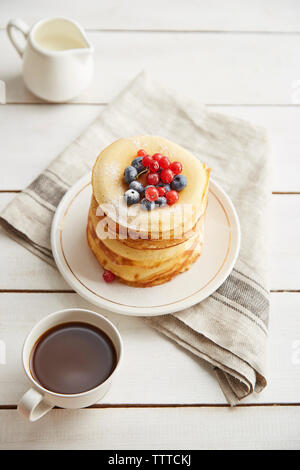 Hohe Betrachtungswinkel der Pfannkuchen in der Platte mit Kaffee und Milch auf hölzernen Tisch serviert Stockfoto