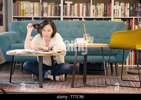 Die volle Länge der jungen Frau Studium, während sie von Sofa auf dem Teppich zu Hause sitzen Stockfoto