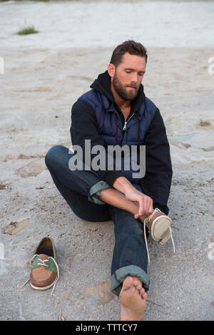 Hohe Betrachtungswinkel des Menschen Schuhe tragen, während am Ufer sitzen Stockfoto
