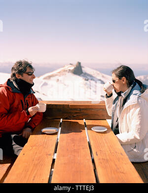 Argentinien, Bariloche, Cerro Kathedrale, glückliches Paar Kaffee trinken im Winter mit Schnee bedeckten Berg im Hintergrund Stockfoto