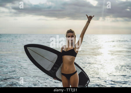 Portrait von zuversichtlich, Frau, tragen, Bikini, während gestikulierte mit Surfbrett im Meer Stockfoto