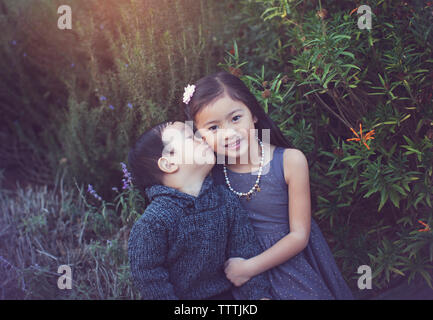 Portrait der netten Schwester mit Bruder sie zu küssen gegen Pflanzen im Park Stockfoto