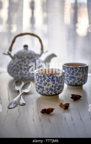 Tasse mit heißem Aufguss von Sternanis und Teekanne auf weiße Holztisch. Stockfoto