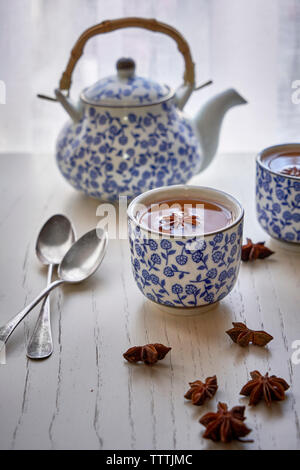 Tasse mit heißem Aufguss von Sternanis und Teekanne auf weiße Holztisch. Stockfoto