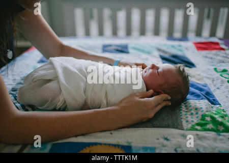 Zugeschnittenes Bild von Mutter berühren gewickelt und Baby im Bett zu Hause Stockfoto