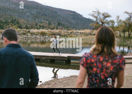 Rückansicht der Eltern auf Sohn läuft auf Pier über den See Stockfoto