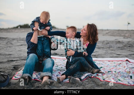 Glückliche Familie sitzen auf Decke am Strand Stockfoto