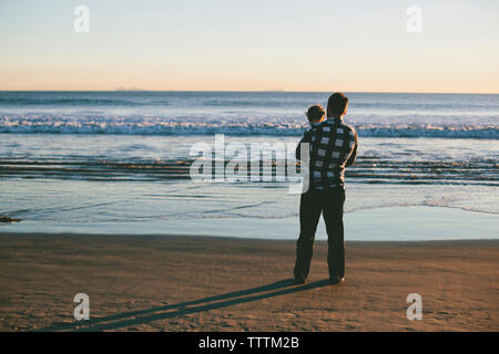 Ansicht der Rückseite des Vater mit Sohn beim Stehen am Strand Stockfoto