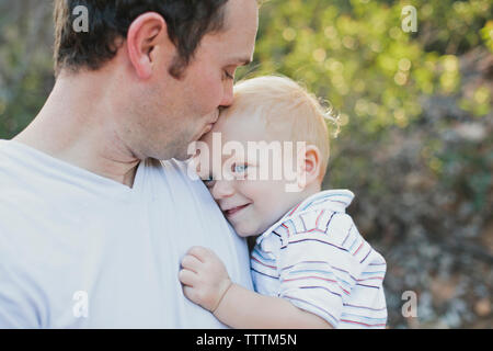 Liebevoller Vater Sohn auf die Stirn Küssen im Park Stockfoto