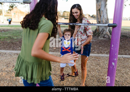 Verspielte Mutter und Tochter spielen mit Mädchen hängen auf Metall am Spielplatz Stockfoto