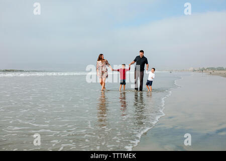 Familie Hand in Hand beim Gehen auf Ufer am Strand gegen Sky Stockfoto