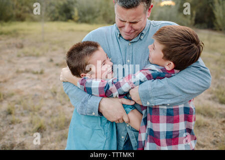 Vater umarmt Söhne beim Stehen auf Feld am Park Stockfoto