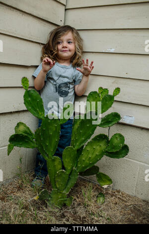 Süße verspielte stehendes Mädchen von Cactus gegen die Wand im Hinterhof Stockfoto