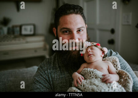 Portrait von bärtigen Vater die niedlichen schlafenden Tochter Tiara tragen, während sie auf dem Sofa zu Hause sitzen Stockfoto