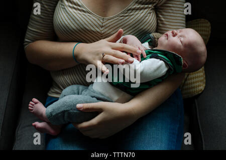 Mittelteil der Mutter sitzen mit niedlichen Neugeborene schlafen Sohn auf Stuhl zu Hause Stockfoto