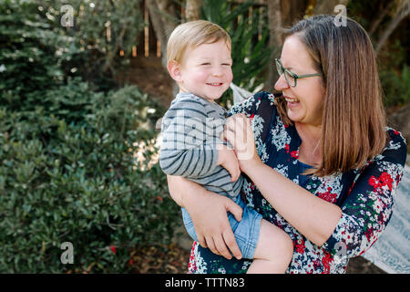 Fröhliche Mutter kitzeln niedlichen Sohn, während ihm im Park tragen Stockfoto