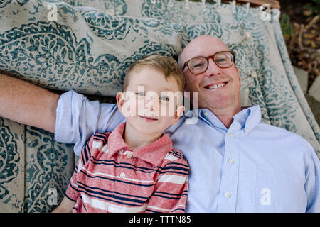 Hohen winkel Portrait von lächelnden Vater und Sohn liegend auf einer Hängematte im Park Stockfoto