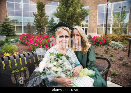 Portrait von Happy Family mit Blumenstrauß sitzt auf der Bank an der Abschlussfeier Stockfoto