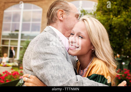 Glückliche junge Frau umarmt Vater auf dem Campus Stockfoto