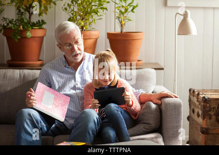 Mädchen mit Tablet-PC beim Sitzen mit Großvater auf dem Sofa zu Hause Stockfoto