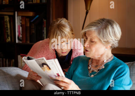 Großmutter lesen Magazin beim Sitzen auf dem Sofa zu Hause Stockfoto