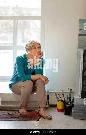 Nachdenkliche Frau weg, beim Sitzen auf der Fensterbank Stockfoto