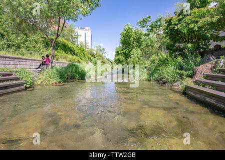 SEOUL, Südkorea - 31. MAI 2019: Zwei Frauen diskutieren auf einer Bank in der Nähe von dem klaren Wasser des Cheonggyecheon Strom, Seoul, Südkorea Stockfoto
