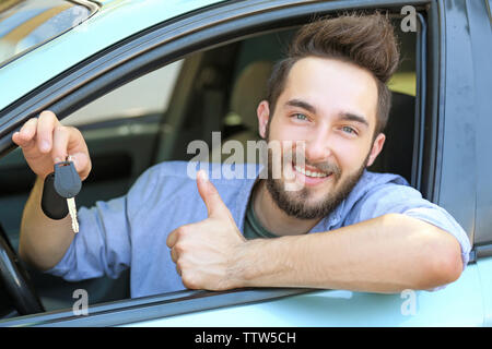 Erfolgreiche junge Mann im Auto sitzen und zeigte mit dem Daumen anmelden Stockfoto