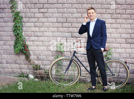 Junger Mann mit Fahrrad sprechen über Mobiltelefon auf der Mauer Hintergrund Stockfoto