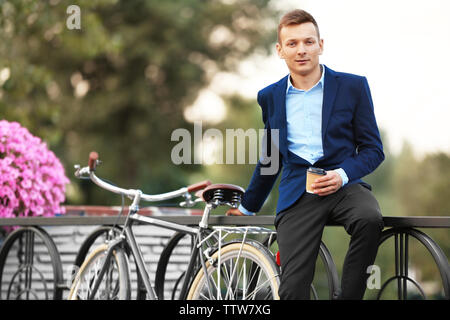 Coffee-to-go-Konzept. Junger Mann mit Fahrrad und Tasse Kaffee auf der Straße Stockfoto