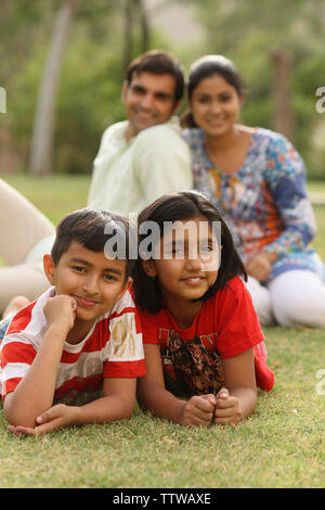 Zwei Kinder liegen auf Gras mit ihren Eltern in der Hintergrund Stockfoto