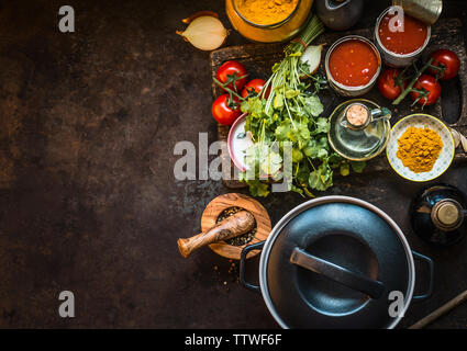 Gesunden Zutaten für leckere Tomatensuppe: Tomaten, frische Kräuter, Gewürze, geschälten Tomaten auf dunklen rustikalen Küche Tisch mit Gusseisen Kochtopf, oben Stockfoto