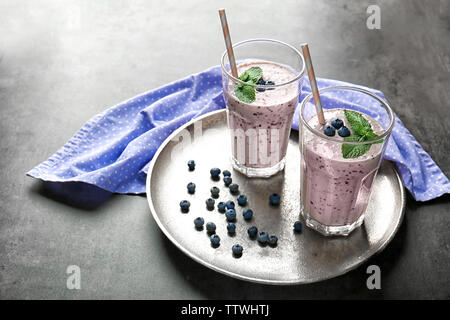 Tablett mit zwei Gläsern leckeren Smoothie, Blaubeeren und Strohhalme auf grau Tabelle Stockfoto